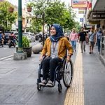 ilustrasi seorang penyandang disabilitas sedang berjalan di trotoar. (Foto: Gemini)